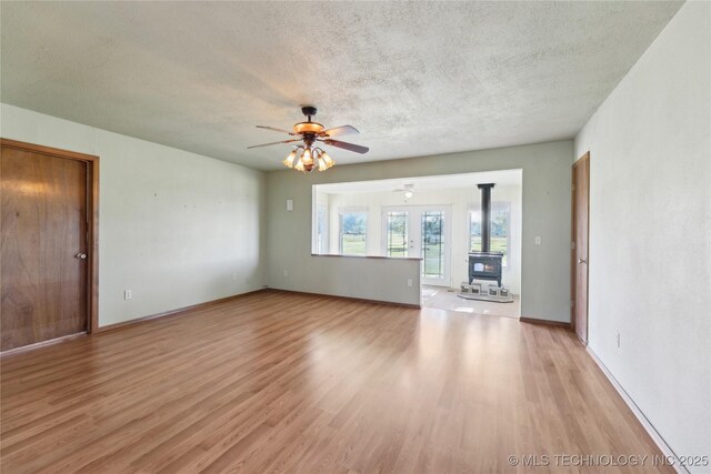 20600 Slick Rd, Kellyville, OK 74039 - unfurnished living room featuring a wood stove, light wood-type flooring, a textured ceiling, ceiling fan, and baseboards