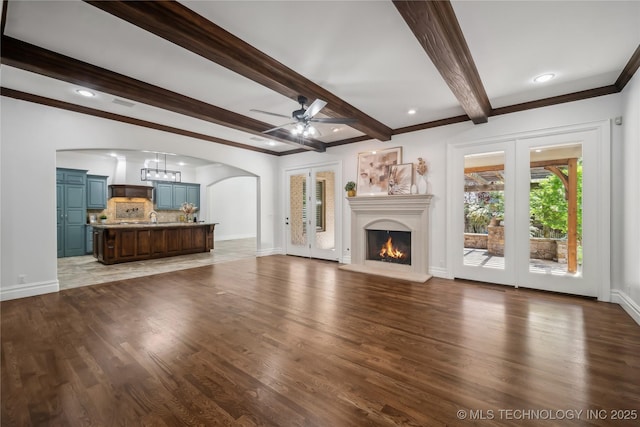 11408 S Harvard Ave, Tulsa, OK 74137 - unfurnished living room featuring arched walkways, ceiling fan, baseboards, beamed ceiling, and wood finished floors