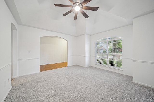 spare room with carpet floors, ceiling fan, arched walkways, vaulted ceiling, and baseboards