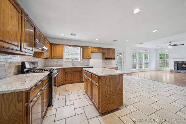 kitchen with stainless steel range with gas cooktop, under cabinet range hood, recessed lighting, brown cabinetry, and backsplash