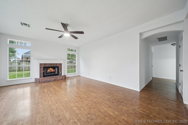 unfurnished living room featuring ceiling fan, wood finished floors, a fireplace, arched walkways, and baseboards