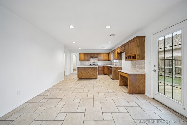 kitchen featuring a center island, recessed lighting, brown cabinetry, light countertops, and decorative backsplash
