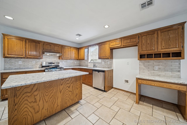 kitchen with appliances with stainless steel finishes, under cabinet range hood, a sink, brown cabinetry, and tasteful backsplash