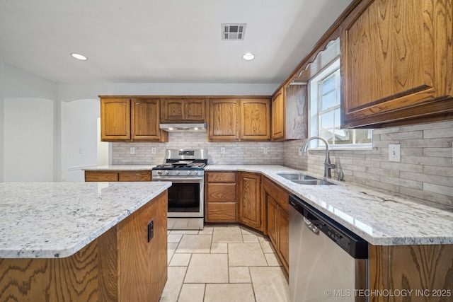 kitchen with stainless steel appliances, exhaust hood, a sink, brown cabinets, and tasteful backsplash
