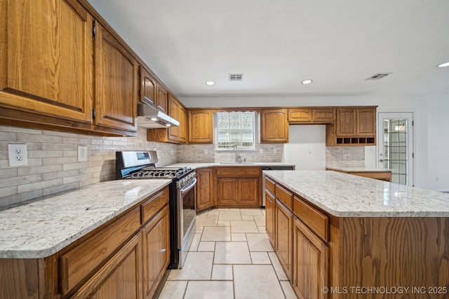 kitchen featuring appliances with stainless steel finishes, under cabinet range hood, a sink, brown cabinets, and backsplash