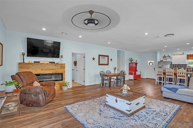 living area featuring wood finished floors, recessed lighting, a glass covered fireplace, and baseboards