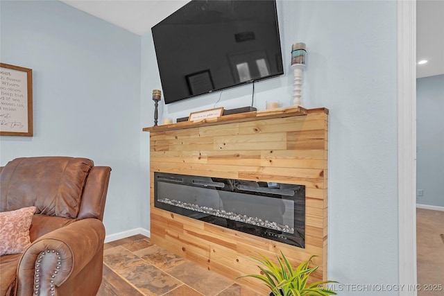 living area featuring a glass covered fireplace, baseboards, and stone finish flooring