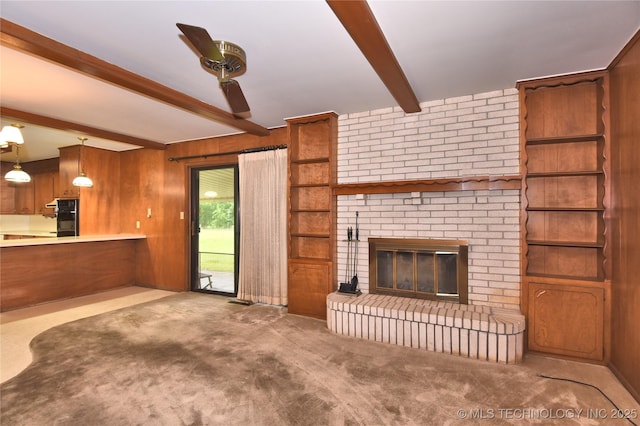 unfurnished living room featuring beam ceiling, carpet flooring, a brick fireplace, and wooden walls