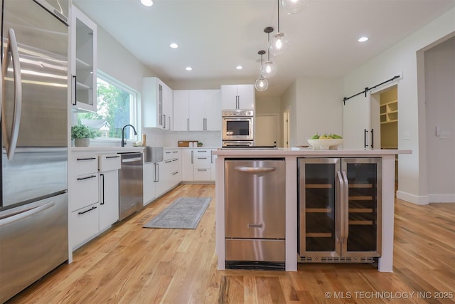2503 S Birmingham Ave, Tulsa, OK 74114 - kitchen with appliances with stainless steel finishes, beverage cooler, a barn door, light wood-type flooring, and recessed lighting