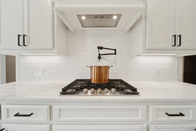 kitchen view of pot filler, stainless steel gas stovetop, white cabinetry, and tasteful backsplash