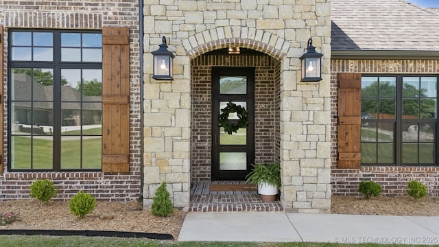 property entrance with brick siding, a shingled roof, and stone siding