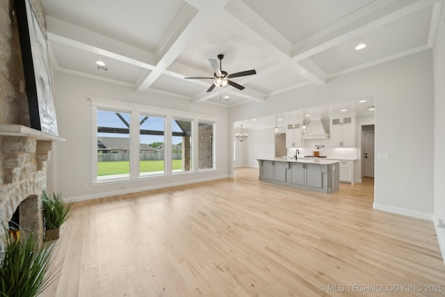 unfurnished living room with a stone fireplace, a sink, coffered ceiling, baseboards, and light wood-style flooring