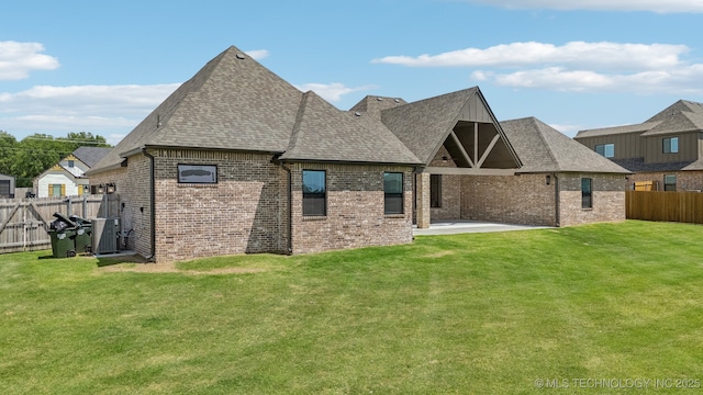 rear view of property featuring brick siding, a shingled roof, and a patio