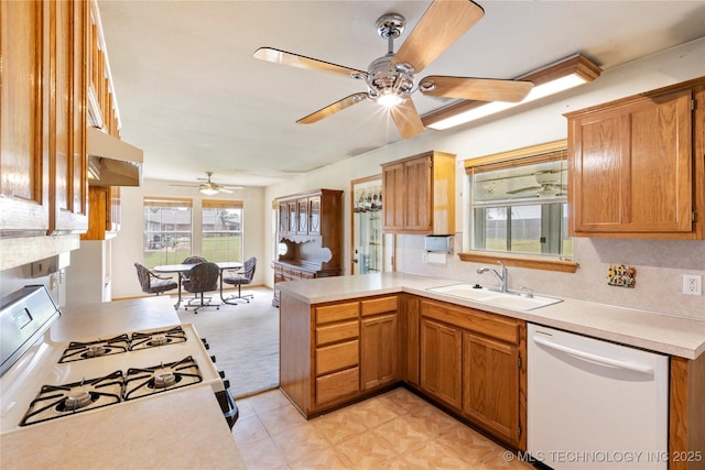 kitchen with white appliances, a sink, a ceiling fan, a peninsula, and light countertops