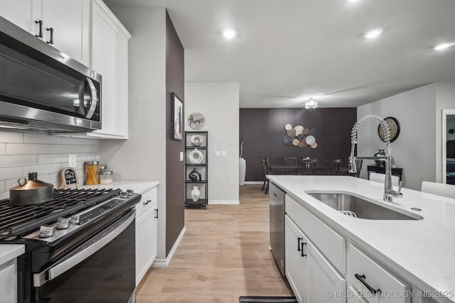 kitchen featuring stainless steel appliances, a sink, decorative backsplash, white cabinetry, and light wood-style flooring