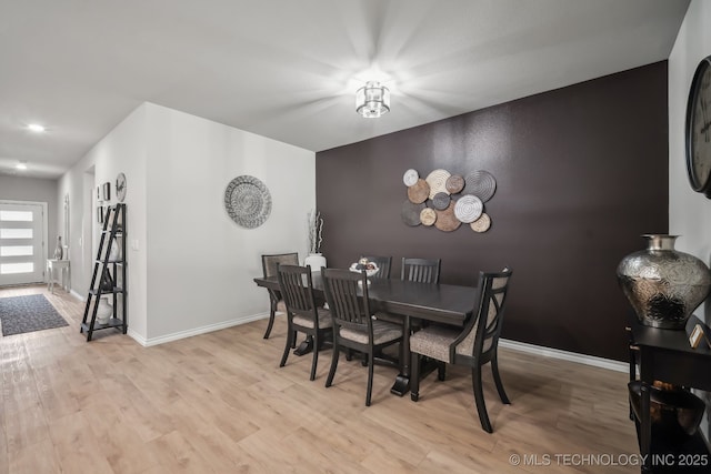 dining room featuring wood finished floors, baseboards, recessed lighting, and an accent wall