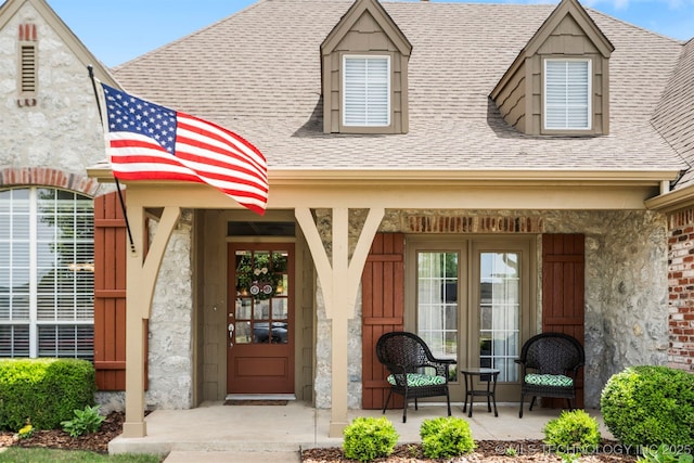 entrance to property featuring covered porch and a shingled roof