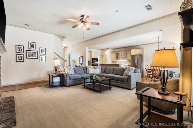 living room featuring ceiling fan, crown molding, stairs, a fireplace with raised hearth, and baseboards