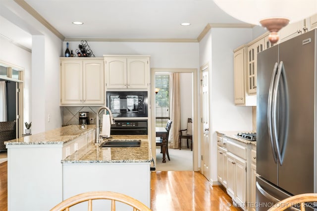kitchen featuring black appliances, light wood finished floors, light stone counters, crown molding, and decorative backsplash
