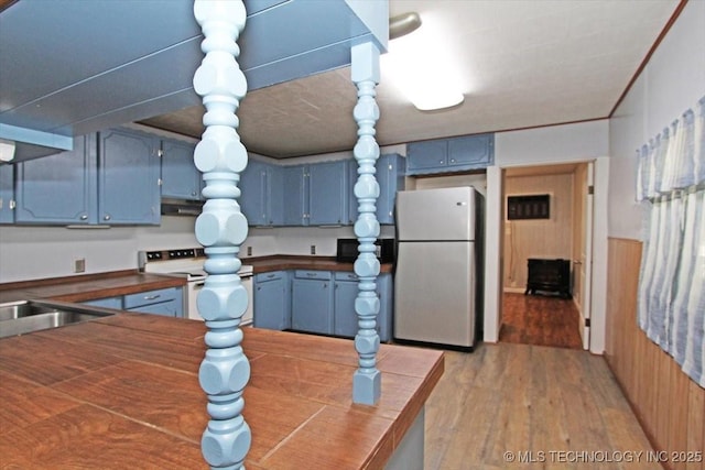 kitchen featuring freestanding refrigerator, electric range, blue cabinetry, dark countertops, and under cabinet range hood