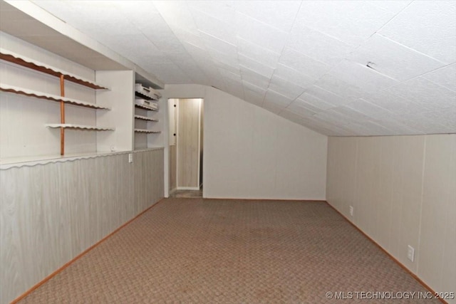 additional living space with carpet floors, lofted ceiling, and wood walls