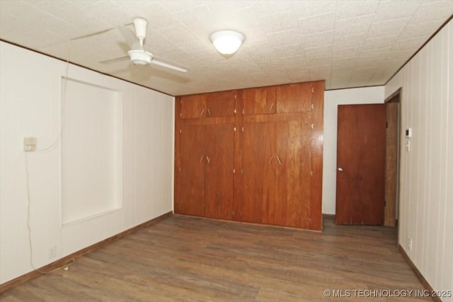unfurnished bedroom featuring wood finished floors, a closet, baseboards, and ceiling fan