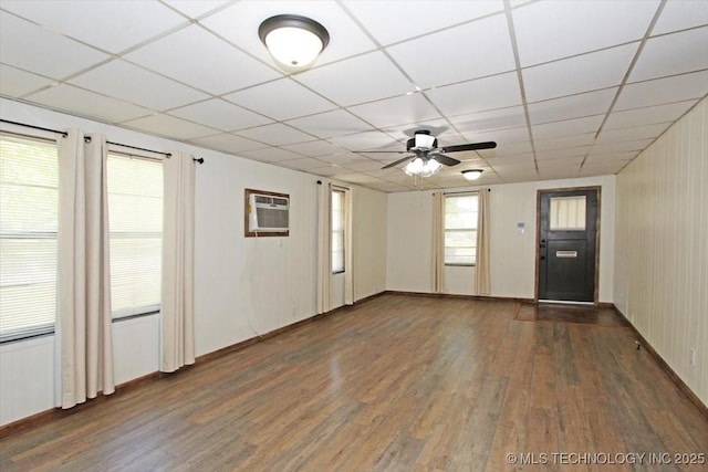 unfurnished room featuring a wall mounted AC, wood finished floors, a paneled ceiling, ceiling fan, and baseboards