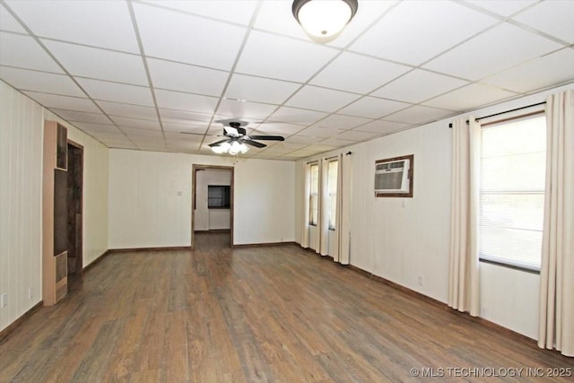 unfurnished room with dark wood-type flooring, a ceiling fan, a drop ceiling, baseboards, and a wall mounted air conditioner
