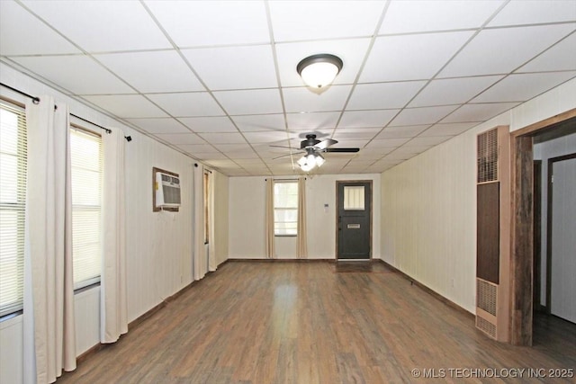 unfurnished living room with a heating unit, wood finished floors, ceiling fan, a wall mounted AC, and a drop ceiling