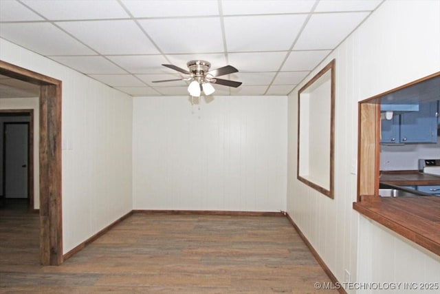 spare room featuring ceiling fan, wood finished floors, a paneled ceiling, and baseboards