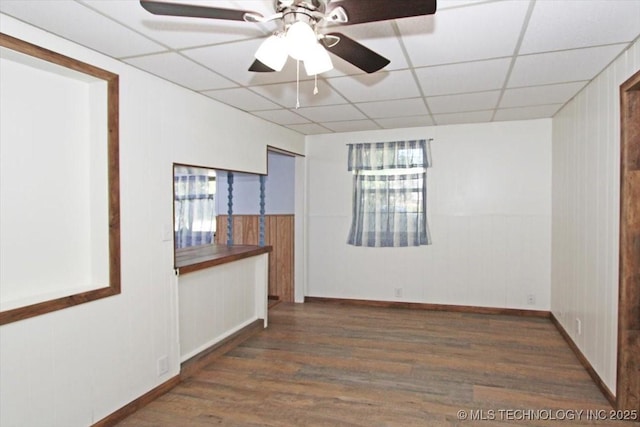 unfurnished room featuring a drop ceiling, wood finished floors, healthy amount of natural light, baseboards, and ceiling fan