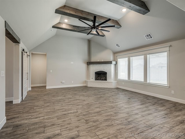 unfurnished living room featuring a ceiling fan, baseboards, a fireplace, a barn door, and wood finished floors