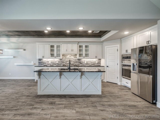 kitchen with appliances with stainless steel finishes, a sink, a raised ceiling, dark stone counters, and recessed lighting