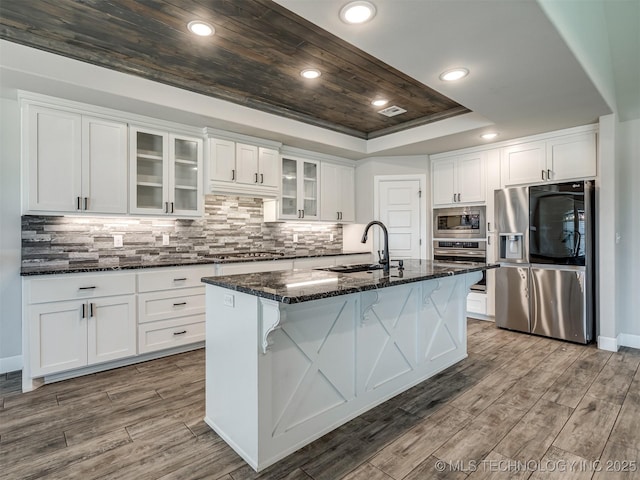 kitchen featuring stainless steel appliances, a sink, a tray ceiling, white cabinets, and dark stone counters