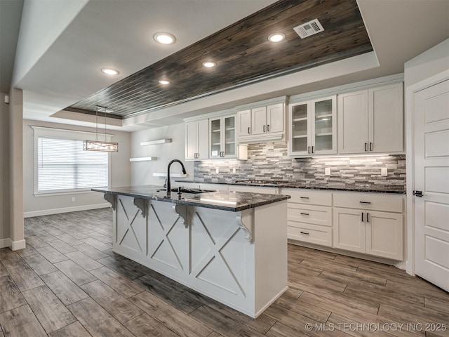 kitchen with a raised ceiling, a sink, dark wood finished floors, white cabinetry, and dark stone counters