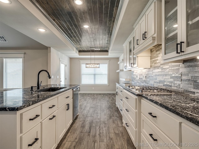 kitchen with a sink, a raised ceiling, baseboards, stainless steel appliances, and dark wood-type flooring