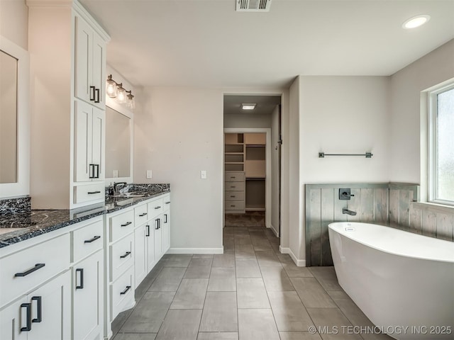 full bathroom with vanity, a freestanding tub, a walk in closet, tile patterned floors, and recessed lighting