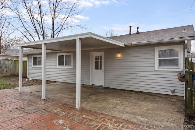 rear view of house with a shingled roof, fence, a patio, and an attached carport