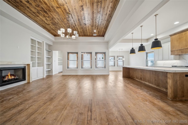 2607 E 135th Dr S, Bixby, OK 74008 - unfurnished living room with a chandelier, built in features, wood ceiling, wood finished floors, and a warm lit fireplace