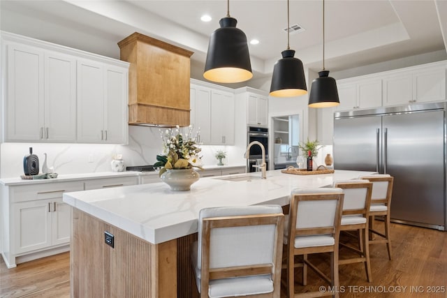 2607 E 135th Dr S, Bixby, OK 74008 - kitchen with appliances with stainless steel finishes, light wood finished floors, white cabinetry, an island with sink, and pendant lighting