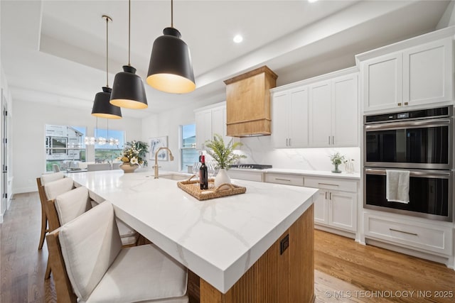 2607 E 135th Dr S, Bixby, OK 74008 - kitchen featuring stainless steel double oven, a kitchen island with sink, gas cooktop, light wood-type flooring, and white cabinets