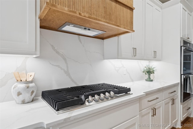 2607 E 135th Dr S, Bixby, OK 74008 - kitchen featuring appliances with stainless steel finishes, range hood, white cabinetry, tasteful backsplash, and light stone countertops