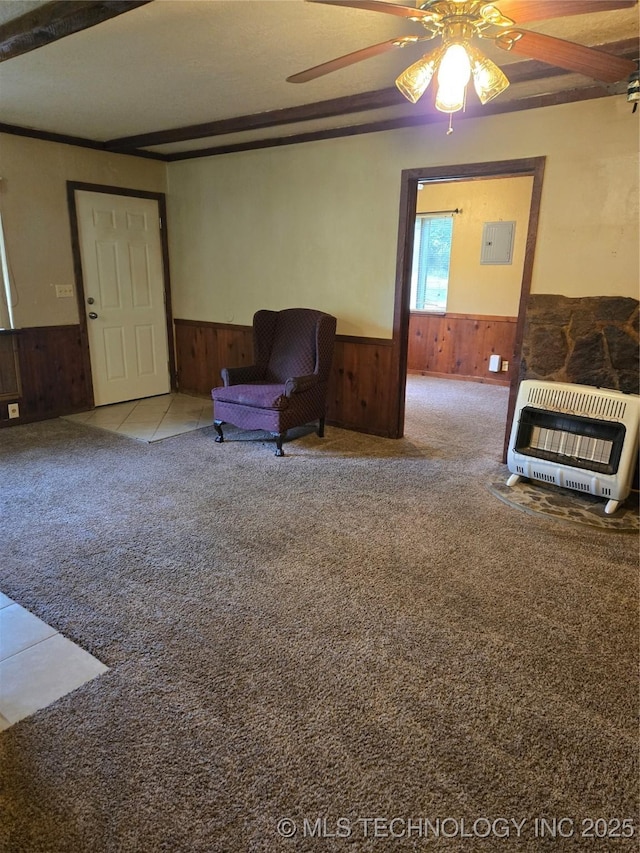 living area with heating unit, wainscoting, wood walls, carpet flooring, and ceiling fan