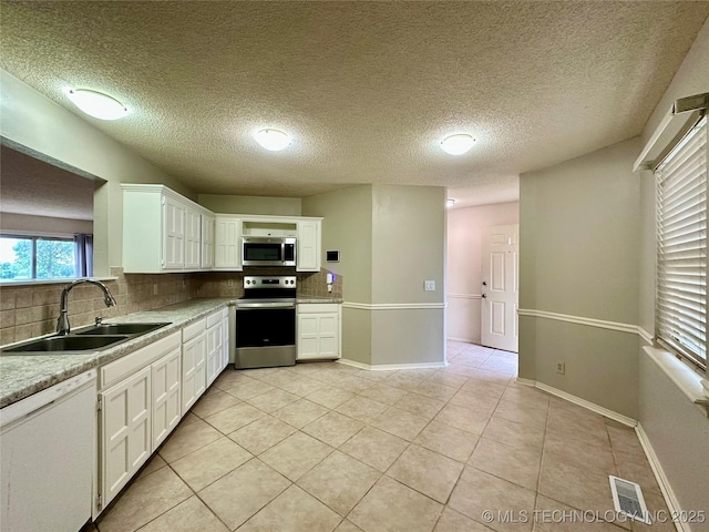 kitchen featuring stainless steel appliances, a sink, backsplash, light tile patterned floors, and a textured ceiling