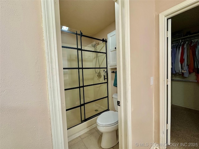 full bathroom with a stall shower, toilet, tile patterned flooring, and a spacious closet