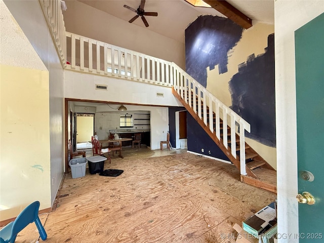 unfurnished living room with high vaulted ceiling, ceiling fan, stairs, wood finished floors, and beamed ceiling