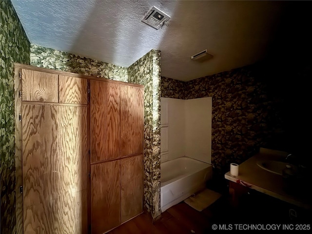 bathroom with wallpapered walls, wood finished floors, vanity, and bathtub / shower combination