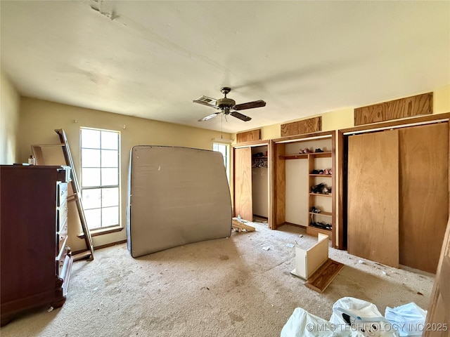 unfurnished bedroom with multiple closets, carpet, and a ceiling fan