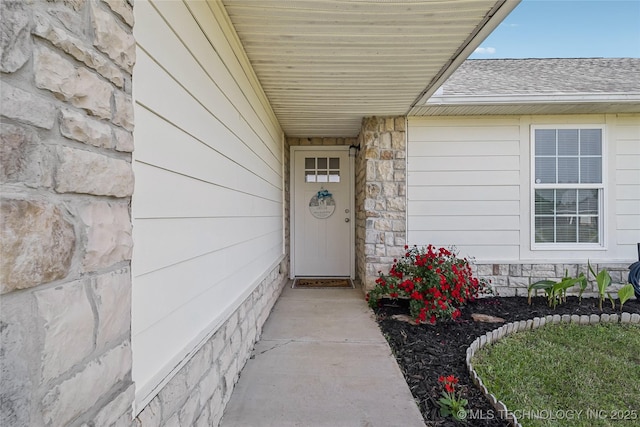 doorway to property featuring stone siding and roof with shingles