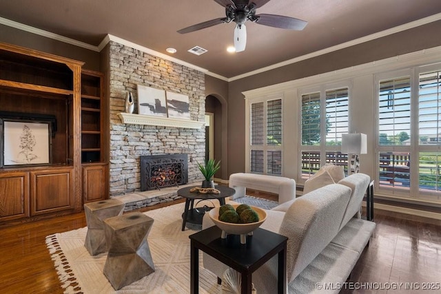 living area featuring plenty of natural light, a fireplace, crown molding, a ceiling fan, and wood finished floors